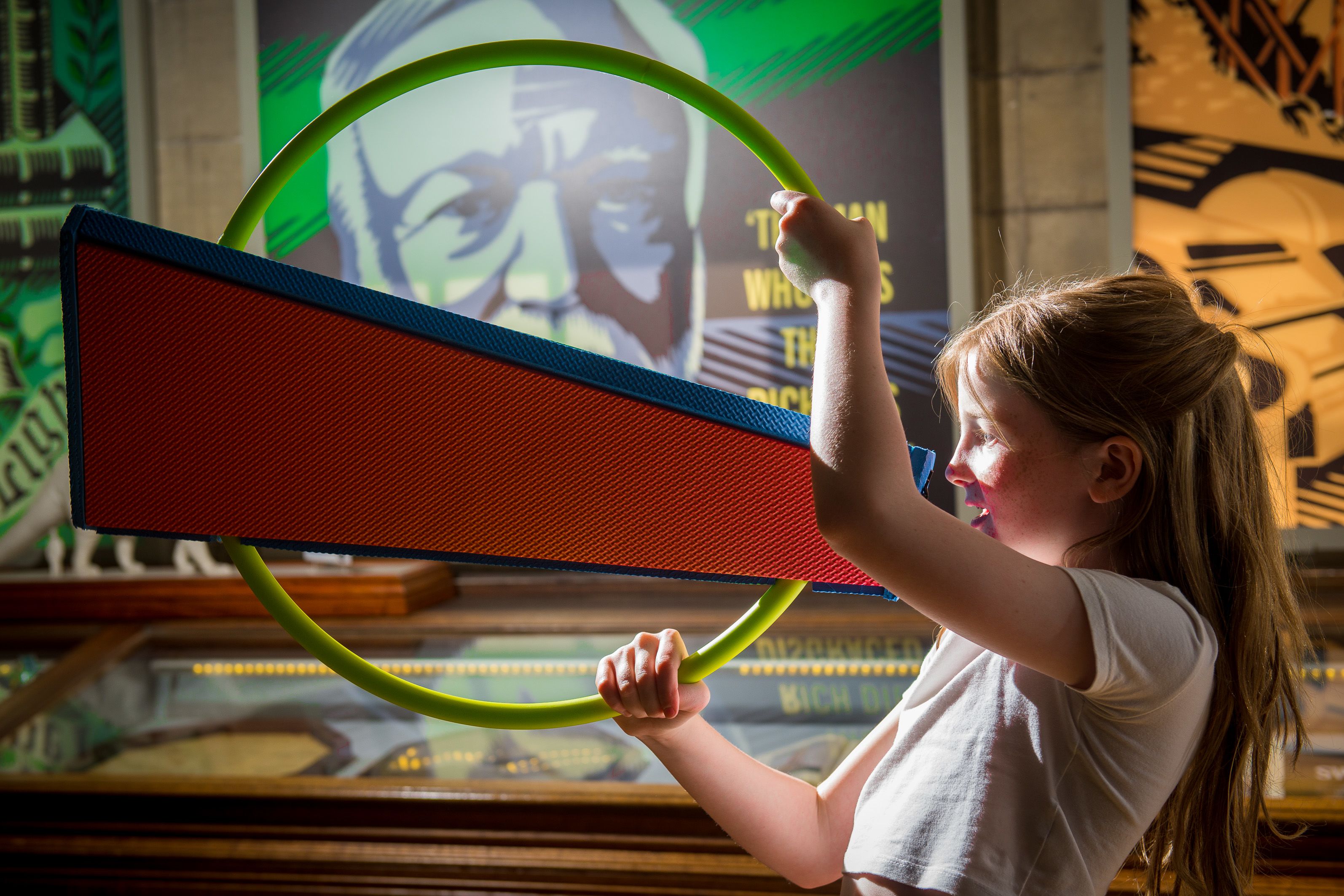 A girl holding a colourful toy loudspeaker in front of a display at the Andrew Carnegie Birthplace Museum.
