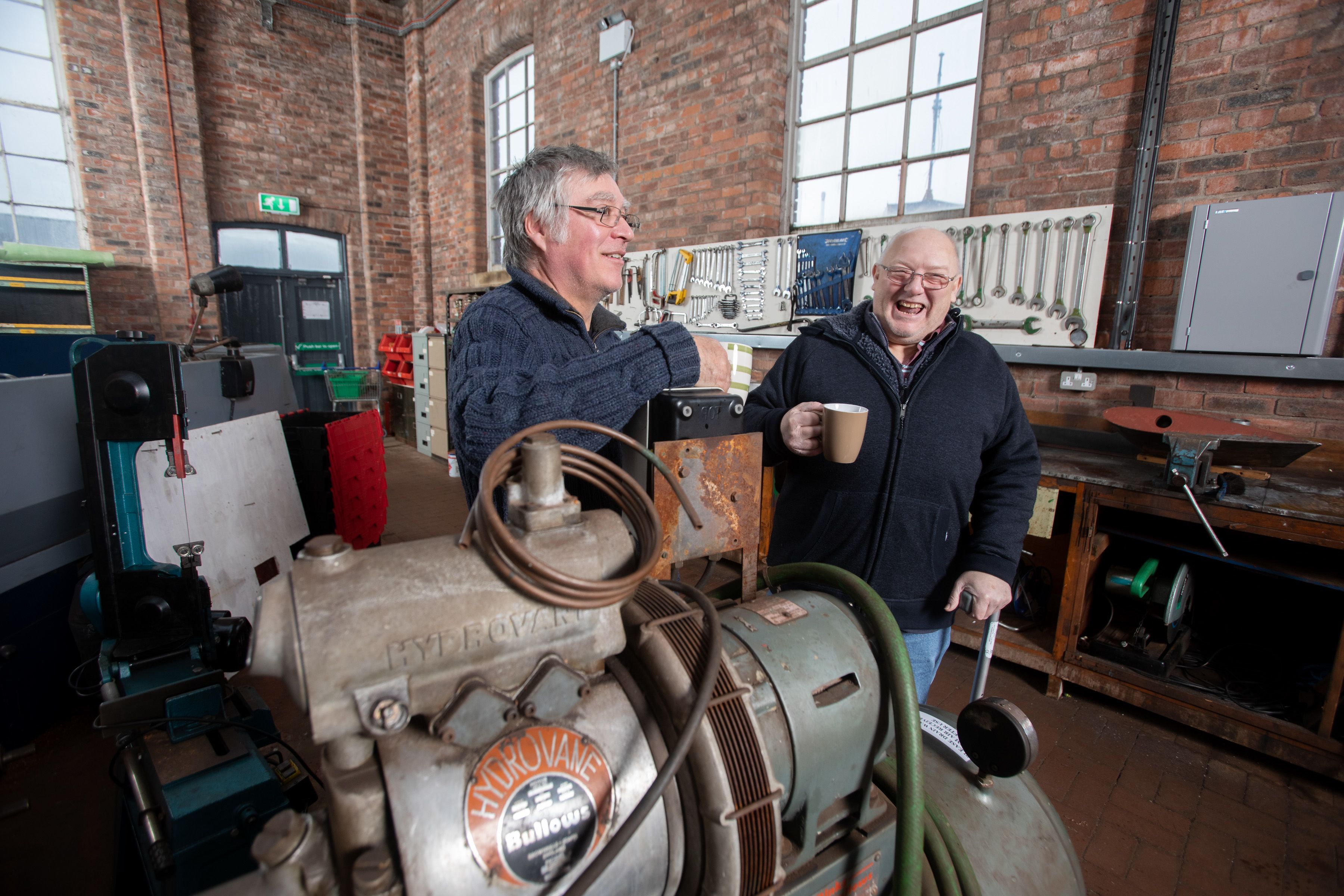 Two men standing with cups of coffee in from of an engine at the Scottish Maritime Museum. Image credit: Martin Shields.