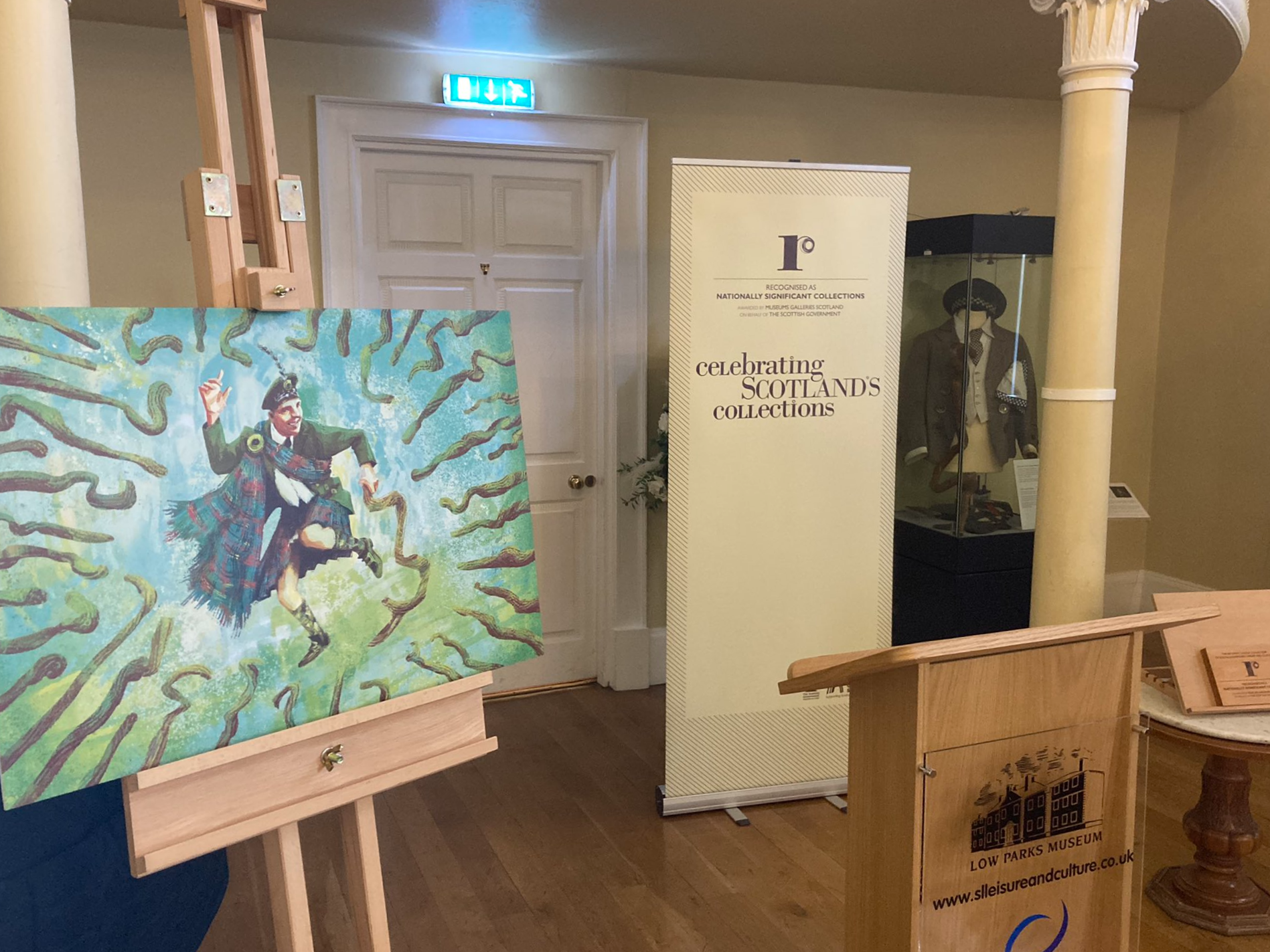 A painting of Sir Harry Lauder rests on an easel next to a lecturn.