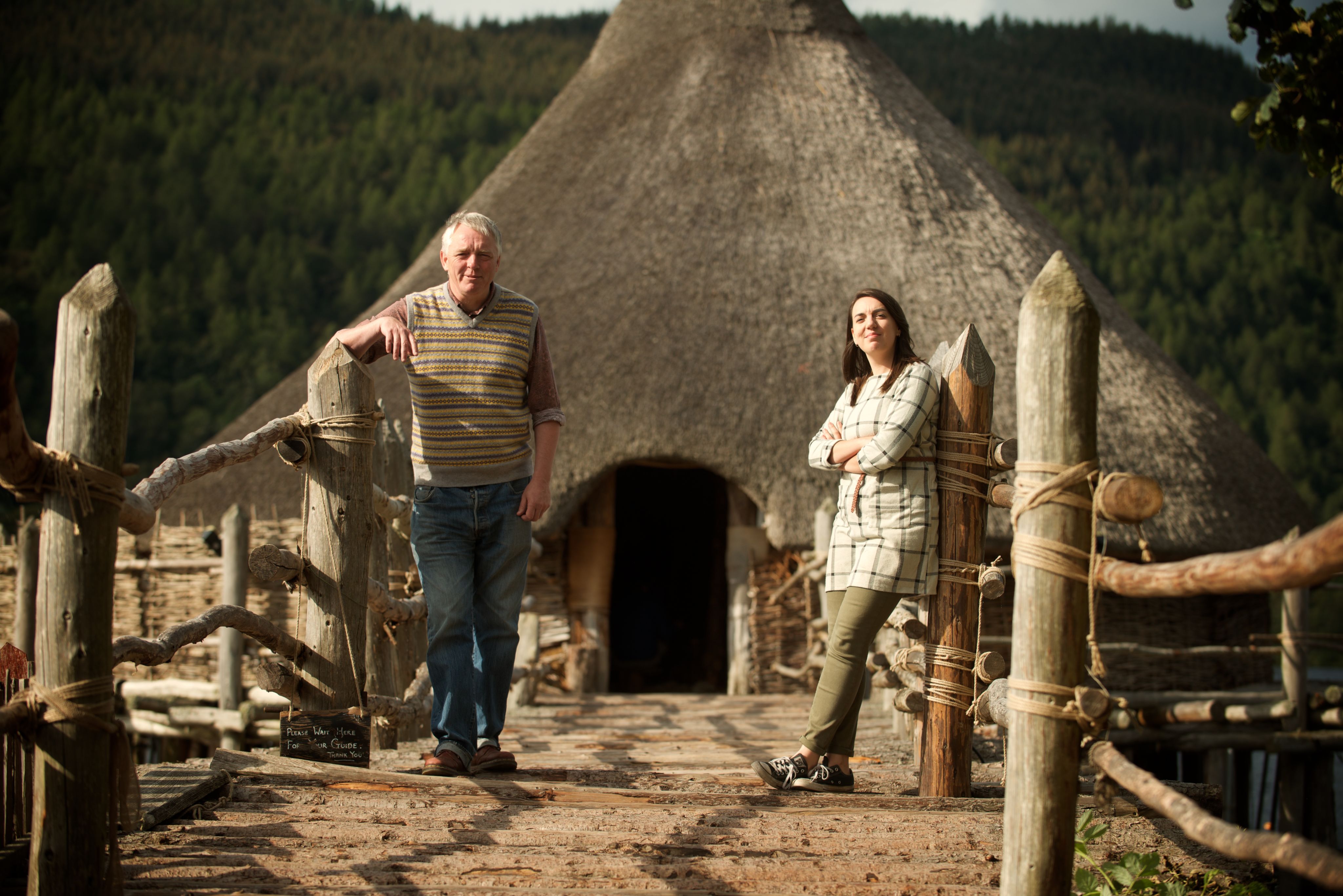 A man and a young woman standing at the entrance to a thatch roundhouse at the Scottish Crannog Centre.